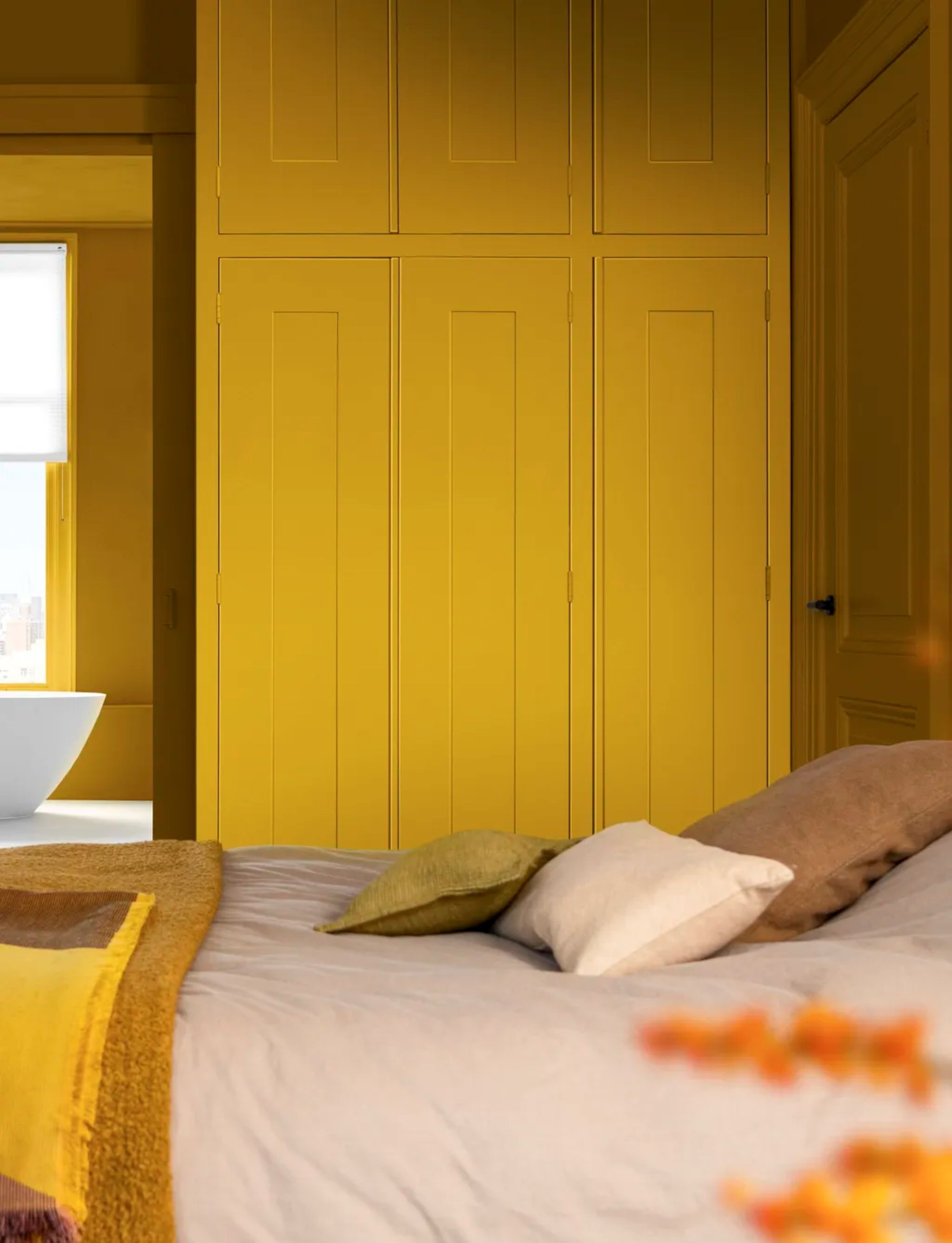 a bedroom with a wall of cabinets painted yellow and a bed with a grey bedspread, a green pillow, a white pillow, and a brown pillow