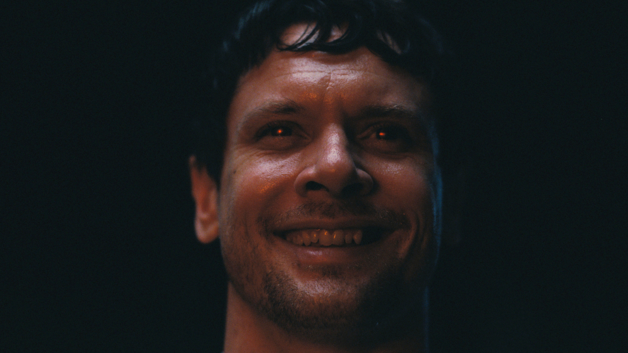 Jack O'Connell smiles gleefully with glowing red eyes in Sinners. 
