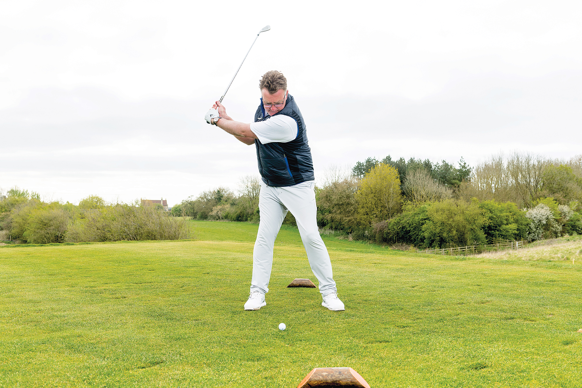 John Jacobs side on hitting an iron shot into the wind, with a shorter swing and the ball position back of stance