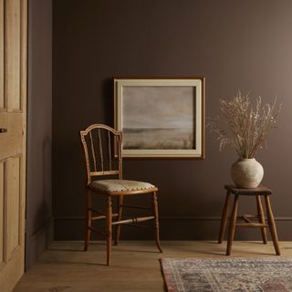 A living space with brown walls, a wooden chair, and a wooden stool with an earthenware vase on it