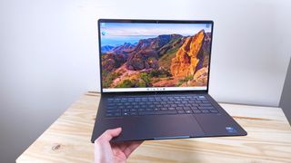 A hand holding up the HP EliteBook Ultra G1i AI with lid open in front of a wood table