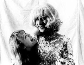 Pamela Des Barres, hugs drummer Keith Moon as he is dressed in drag of a blonde wig and a sequined gown backstage at a KROQ concert in 1972 in Los Angeles, California