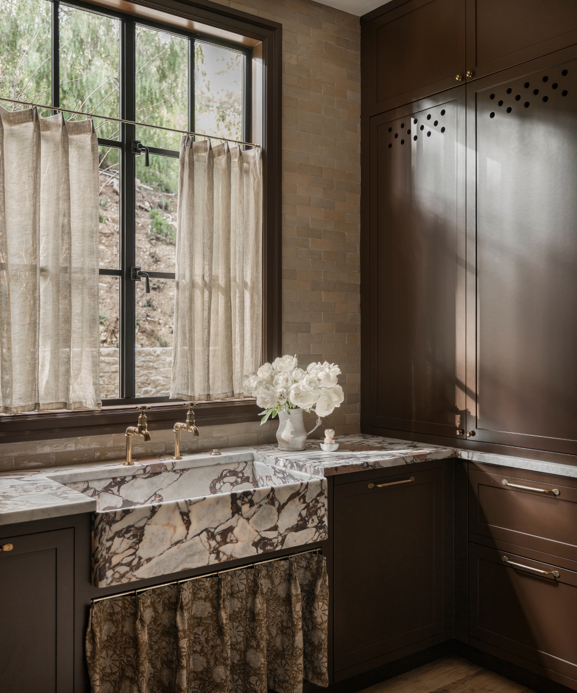 A dark brown kitchen with statement marble countertops that wrap around the sink