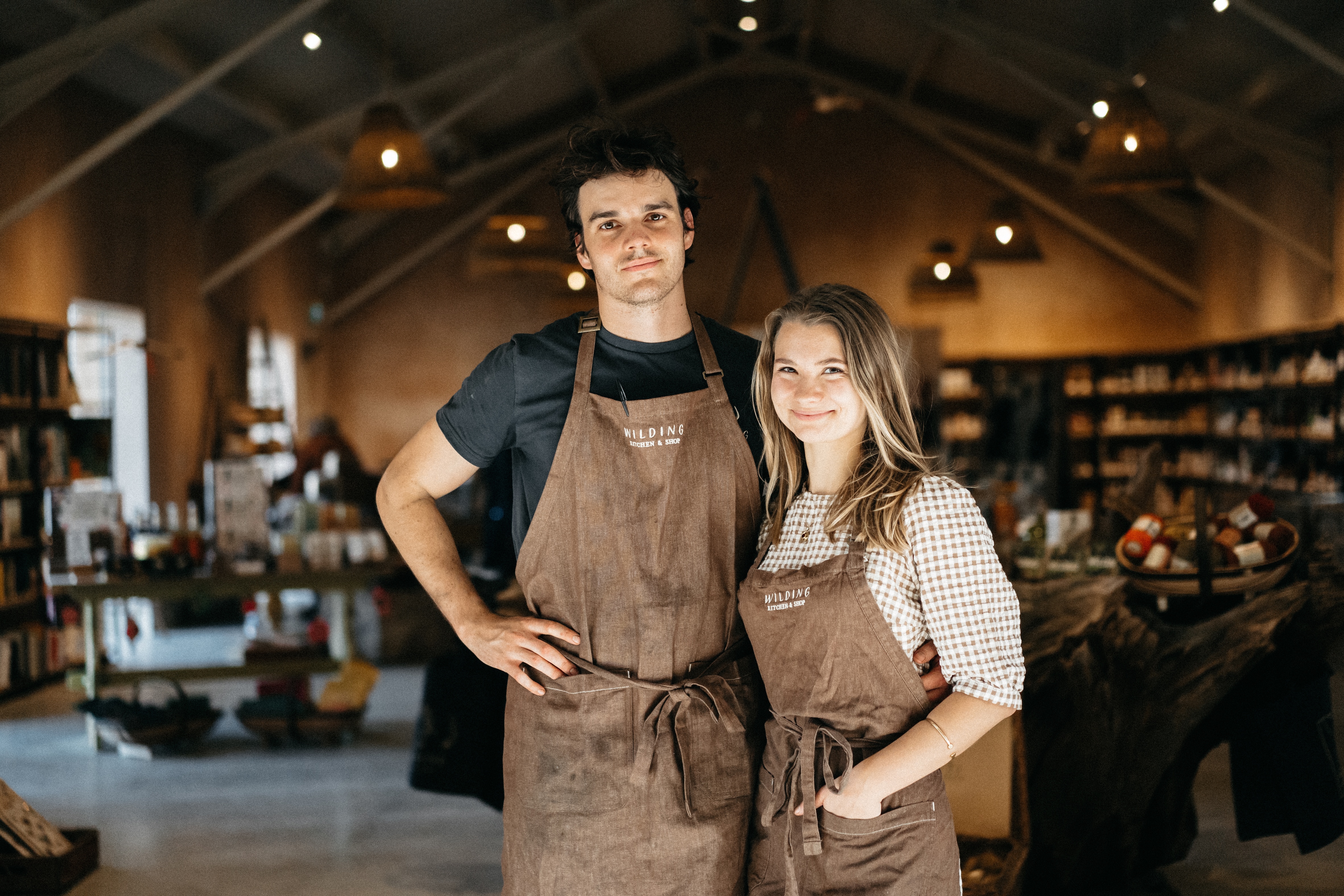 A man and woman standing with their arms around each other, dressed in brown aprons