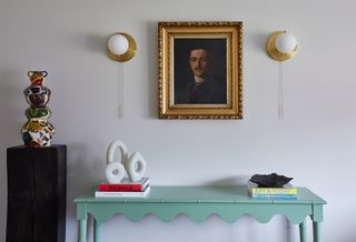 a green console table with arts and wall sconces above