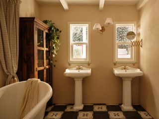A bathroom with checkerboard tile flooring, a large bath, and double pedastal sinks