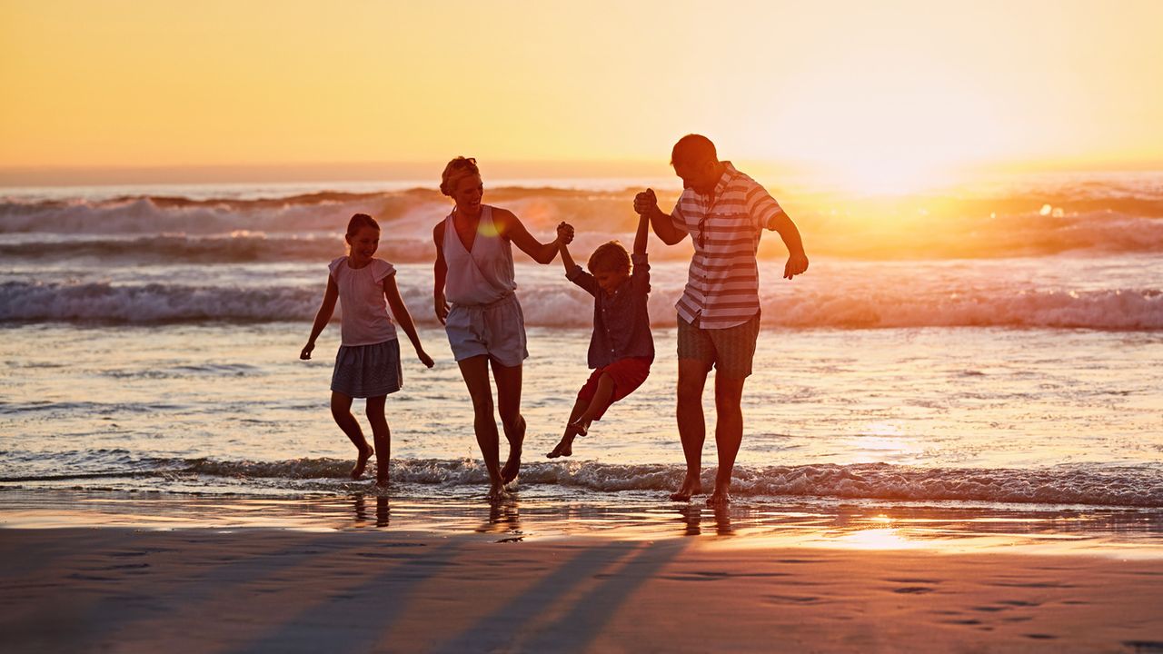 Full length of parents with children enjoying vacation on beach during sunset