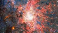 This image features data from Webb&rsquo;s MIRI (Mid Infrared Instrument) to capture the most detailed mid-infrared view yet of the field that hosts the highly evolved star IRS 3, which is located just 0.55 light-years from Sagittarius A*, the Milky Way galaxy's central supermassive black hole.&nbsp; An international team of astronomers have discovered that dust and water can form and survive surprisingly close to this supermassive black hole. The observations reveal that the evolved star IRS 3 continues to enrich its surroundings with newly formed material despite the intense radiation environment around Sagittarius A*. [Image description: A bright, densely populated star cluster lies near the centre of the image, surrounded by intricate clouds of glowing gas and dust in shades of red, pink, orange, and blue. Dark lanes of dust weave through the nebula, contrasting with the luminous central region. Countless stars are scattered across the field, with a few brighter foreground stars showing Webb's characteristic diffraction spikes. An irregular black region occupies the lower-right corner of the image, indicating an area where no observational data was available.]