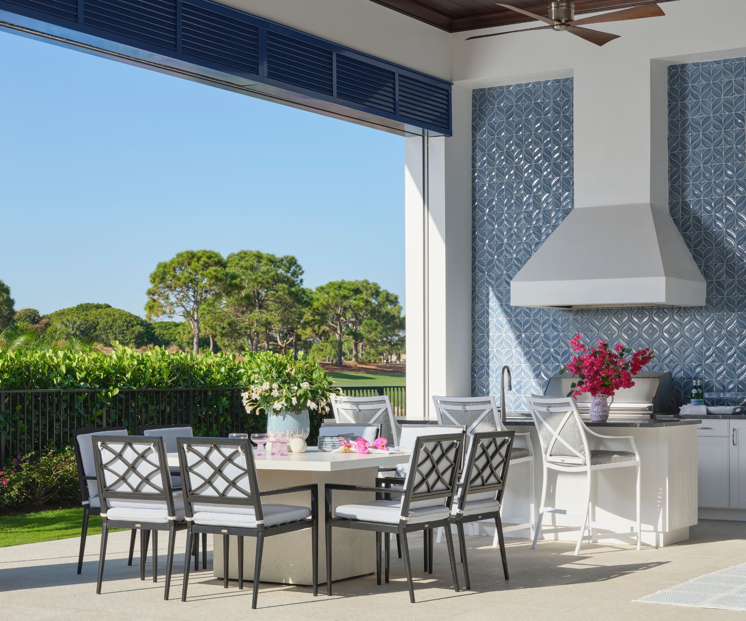 A covered outdoor kitchen with tiles walls, white cabinets, black countertops, and stainless steel appliances
