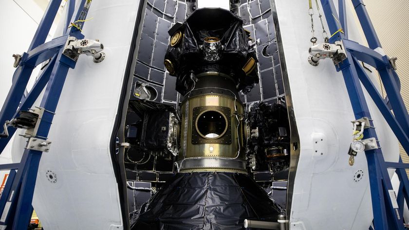 A large metal cylinder covered with black plastic is stood between blue scaffolding.