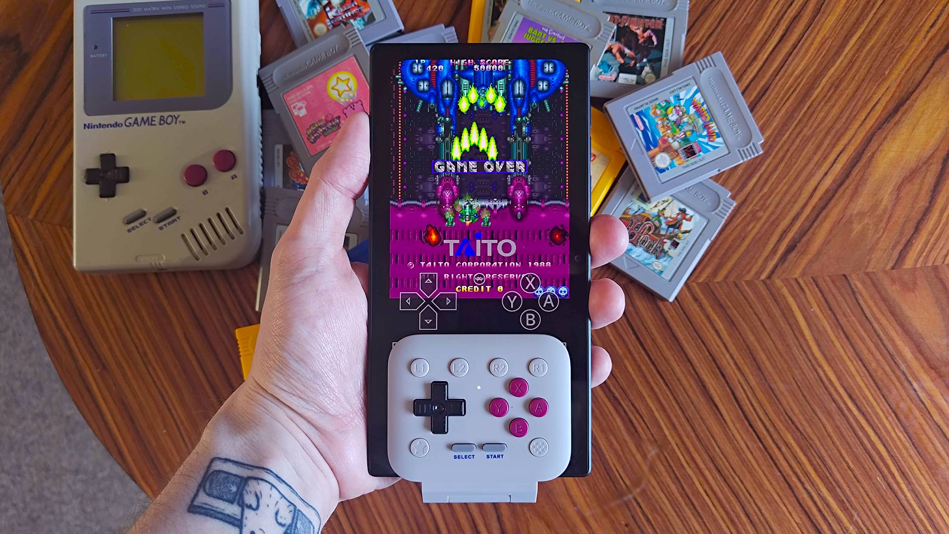 Hand holding Razer Edge with 8Bitdo FlipPad Game Boy controller connected vertically and Truxton demo on screen.