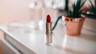 tub of red lipstick sat on a white dressing table, with plant in the background