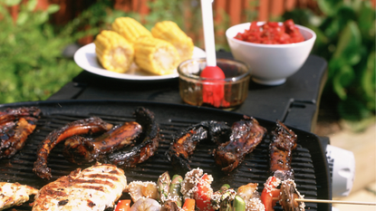 BBQ food on grill and sweetcorn cobs on white plate