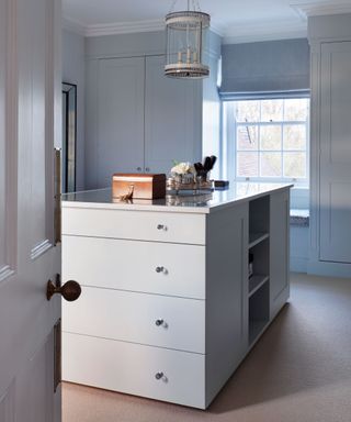 A pale blue-gray walk-in closet idea with white drawers and a sash window.