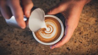 Hands pouring milk froth into cup of coffee