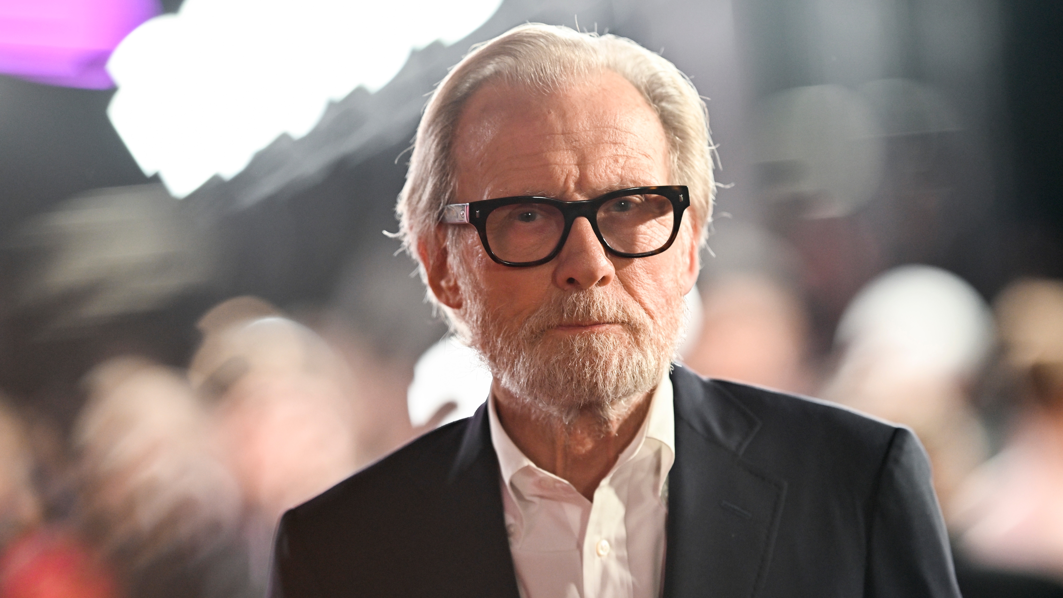 Bill Nighy attends a premiere in a white shirt and black jacket and also a dark framed pair of glasses. 