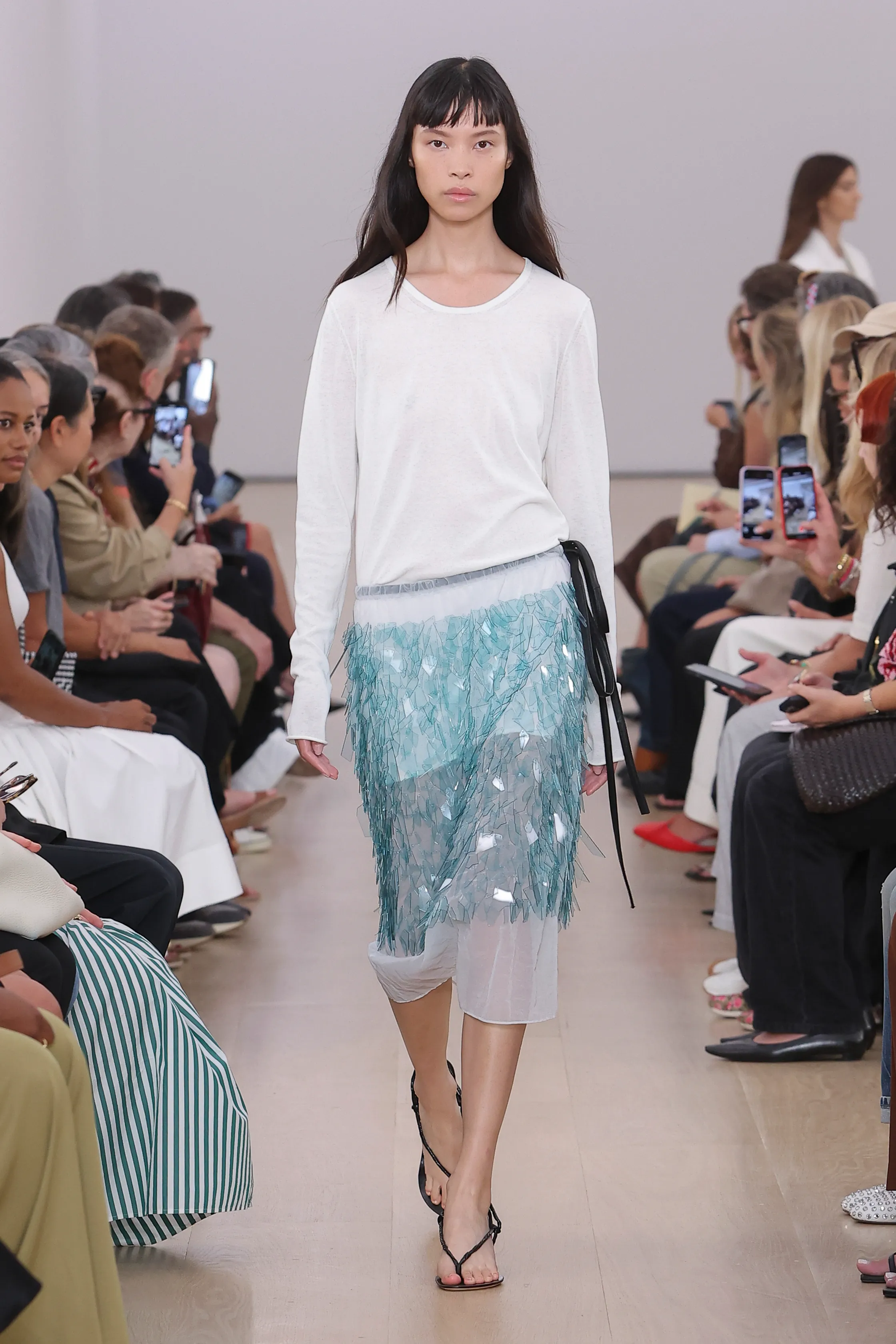 A model in Proenza Schouler Spring 2024 wearing a sheer skirt and white top.