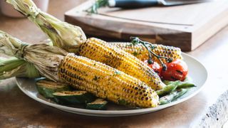 A plate of corn grilled in the jusk with zucchini and tomatoes