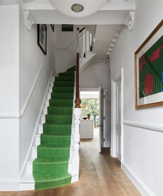 White hallway and staircase with bright green stair carpet and ornate coving and plasterwork