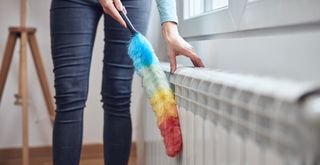 Person with a rainbow colored feather duster cleaning a radiator to show how to get rid of dust in the home