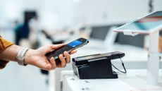 A woman holds her smartphone near a credit card machine while shopping.