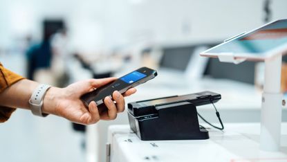 A woman holds her smartphone near a credit card machine while shopping.