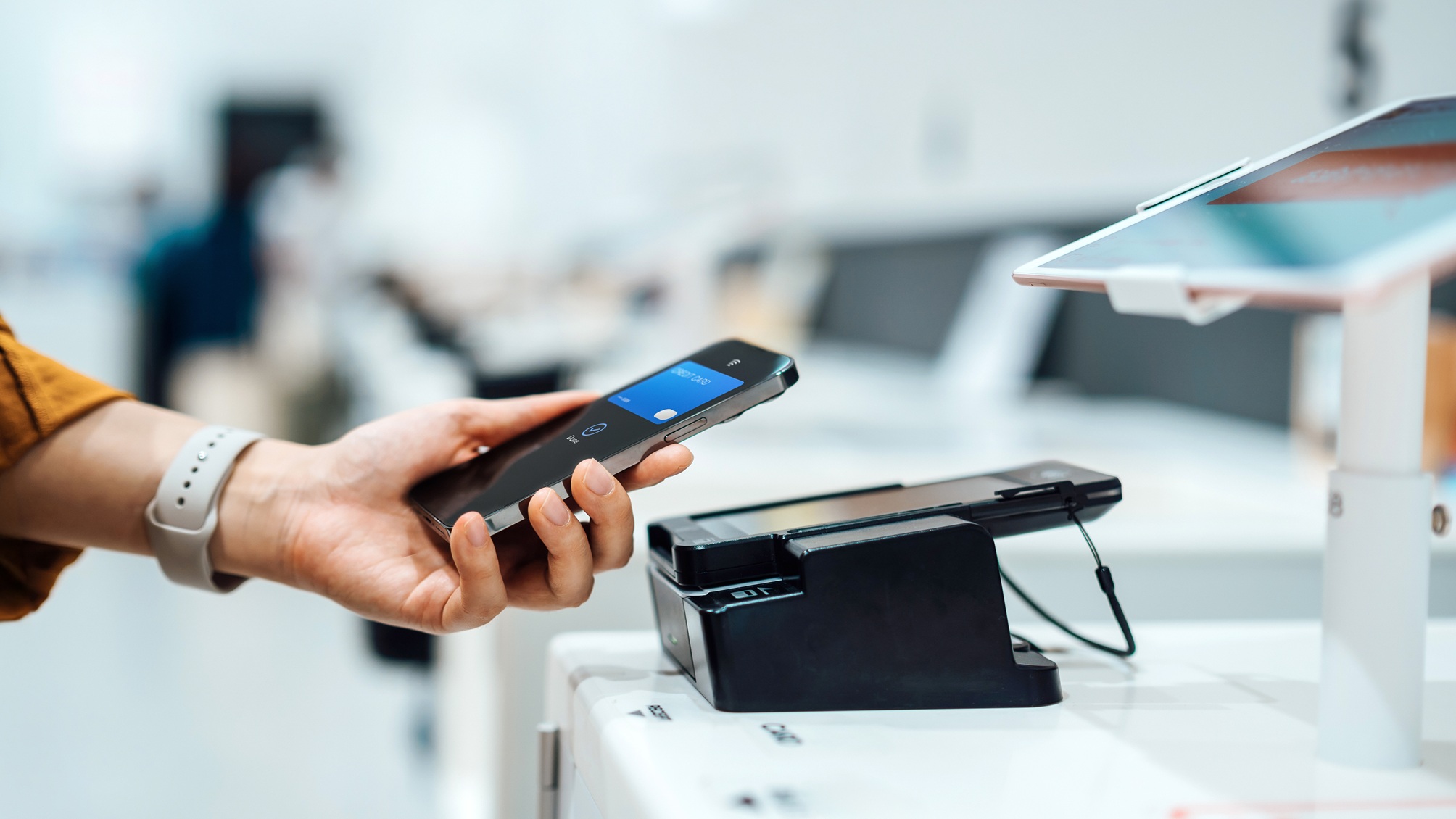 A woman holds her smartphone near a credit card machine while shopping.
