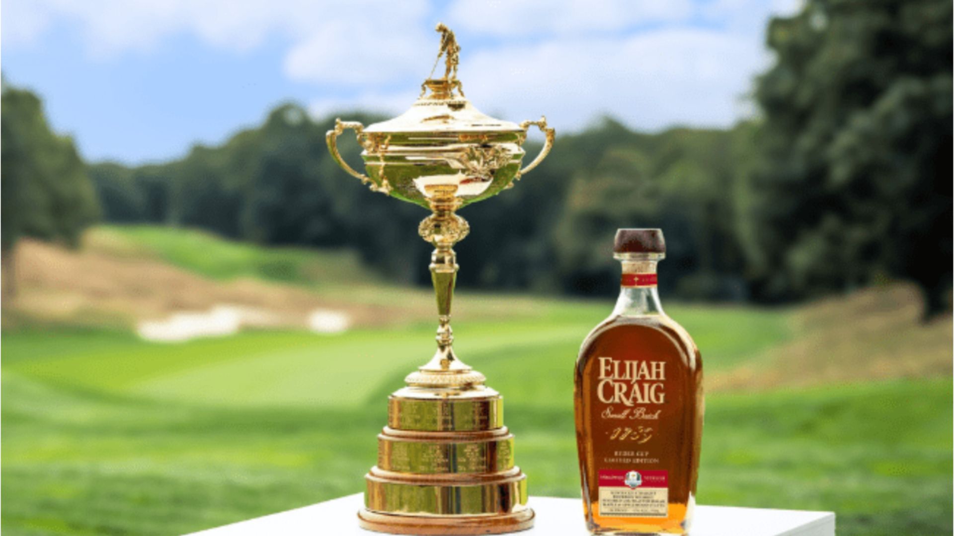 an image of the elijah craig ryder cup special bourbon on a white plinth next to the ryder cup trophy