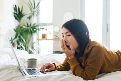 Exhaustion symptoms: Young woman yawning when using laptop working from home