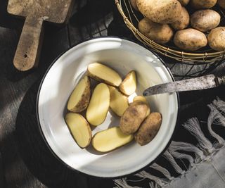 Slices of potato in a white ceramic bowl next to a rustic chopping knife on a black surface