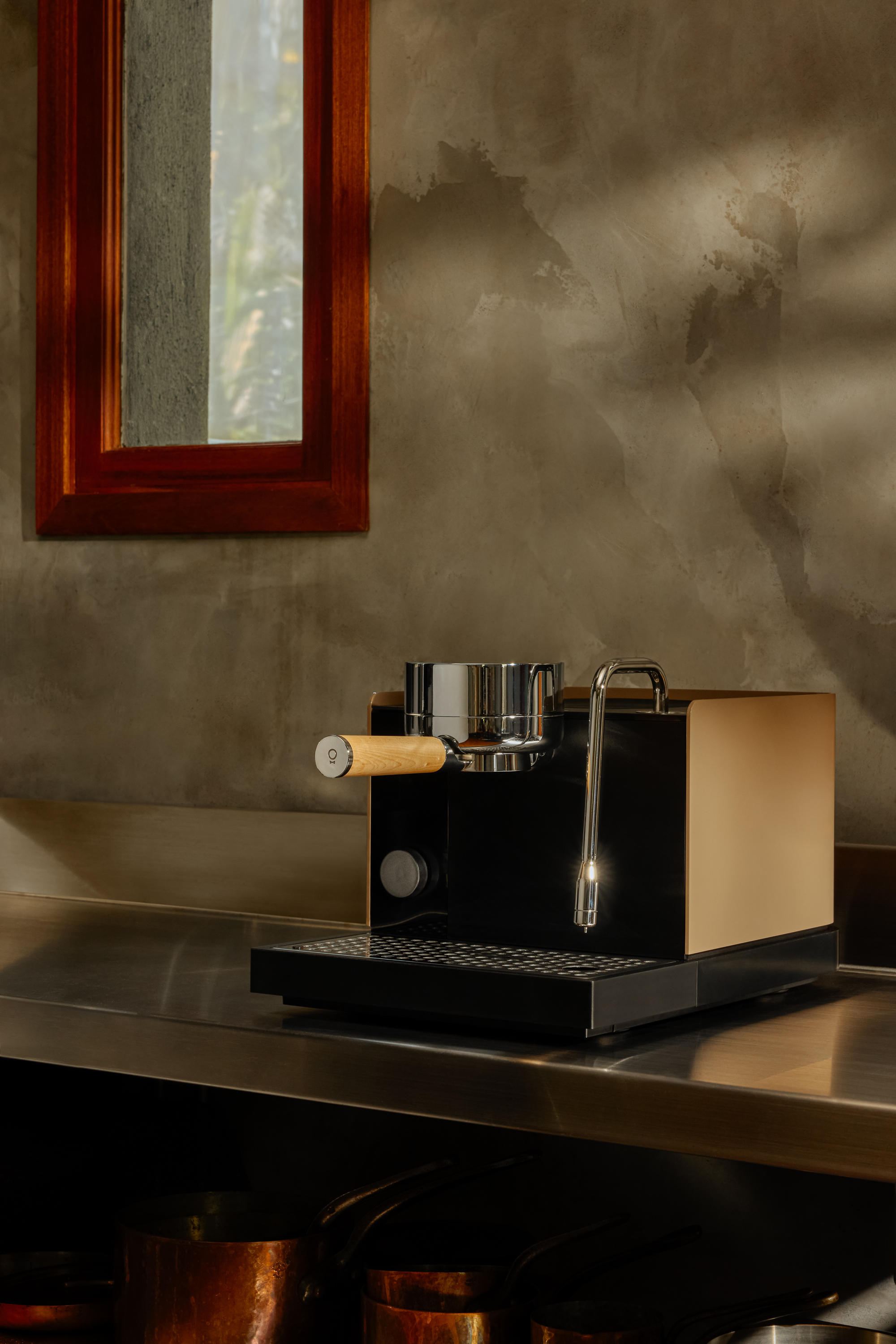 Image of a black and tan espresso machine on a chrome countertop in a room that is painted with gray limewash.