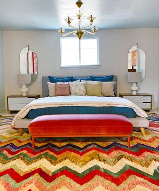 colorful bedroom with multi-colored zig-zag carpet, red ottoman, large bed and neutral walls