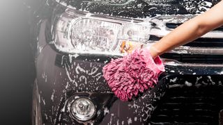 Someone cleaning a soapy car with a mitt