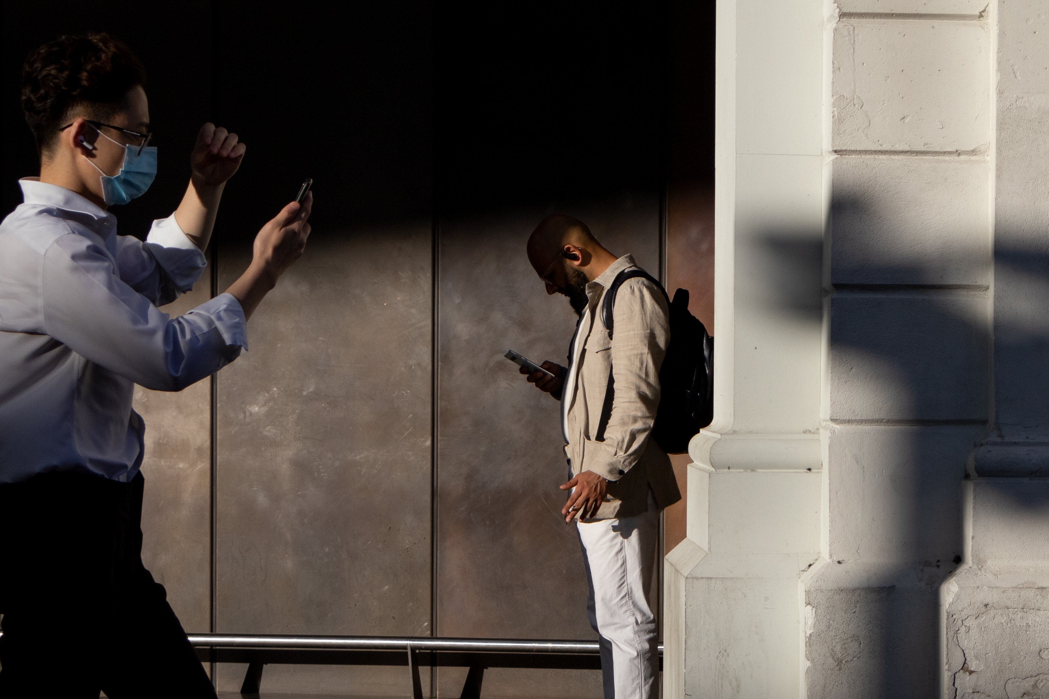 Человек стоит в тени на станции и читает свой телефон
