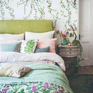 A bedroom with a foliage-print wallpaper and a green fabric headboard on the bed