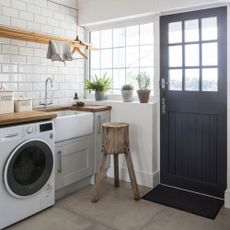 White utility room with white tiles and grey cabinets, with an integrated washing machine 