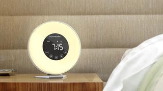 The image shows the HomeLabs Sunrise Alarm Clock on a bedside table in a neutral bedroom