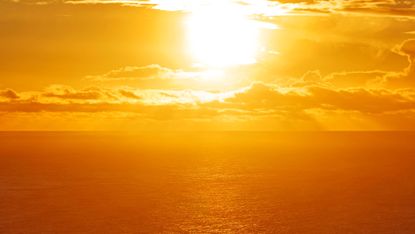 A blazing sun beats down on the ocean and colors it orange.