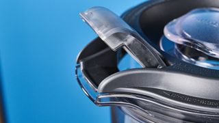 a black nutribullet with a big blending component is photographed in front of a blue backdrop, showing its plastic pitcher jug, silver blades, and tamper