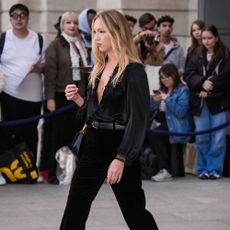 Lila Moss wears black flared jeans with a black blouse and heeled platform boots.