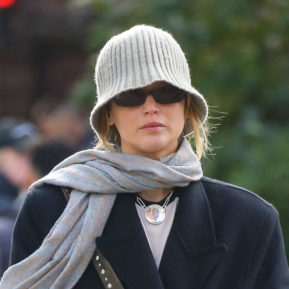 Jennifer Lawrence wearing a knit beanie, oversized coat, scarf, flats, and suede studded bag in NYC