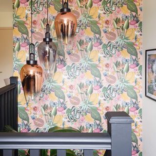 Staircase with brightly coloured tropical wallpaper and three metallic pendant lights