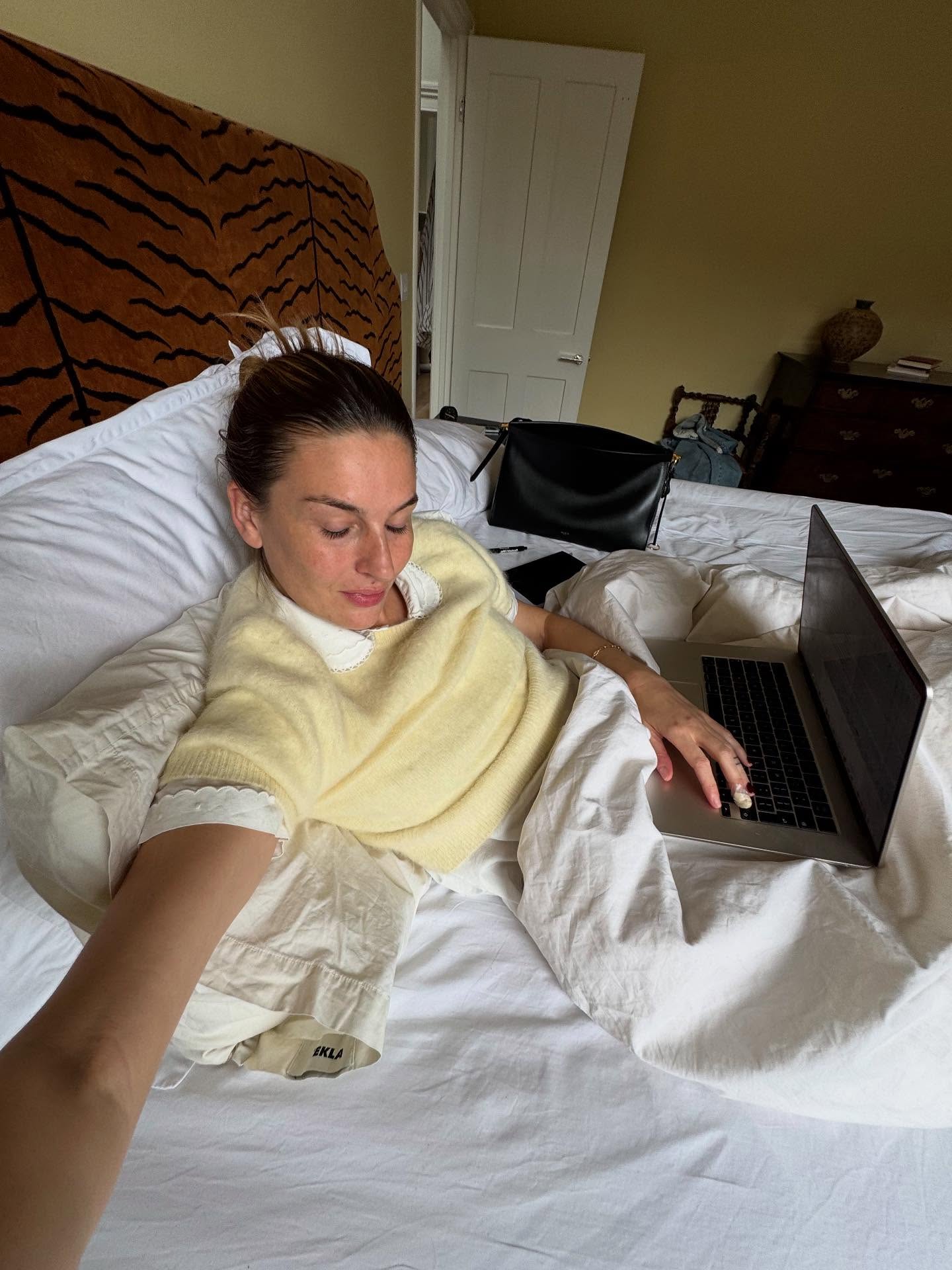 Woman in pale yellow sweater sitting in bed with a computer