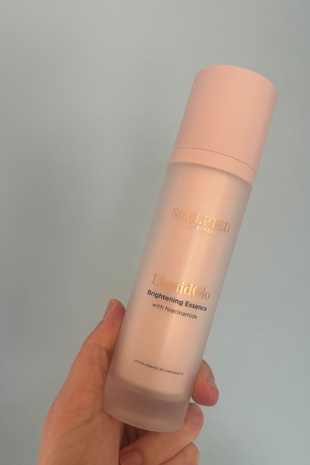a hand holding a bottle of sculpted by aimee liquidglo beauty essence