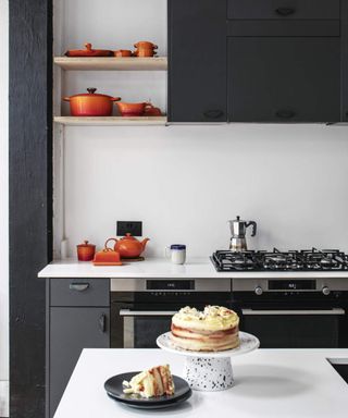 A sponge cake presented on a cake stand with sliced cake on plate in kitchen with stovetop, moka coffee maker and ombre cookware in background - (V46009)