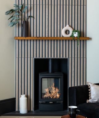 A wood burning stove in a mantle place tiled with vertical stripe tiles