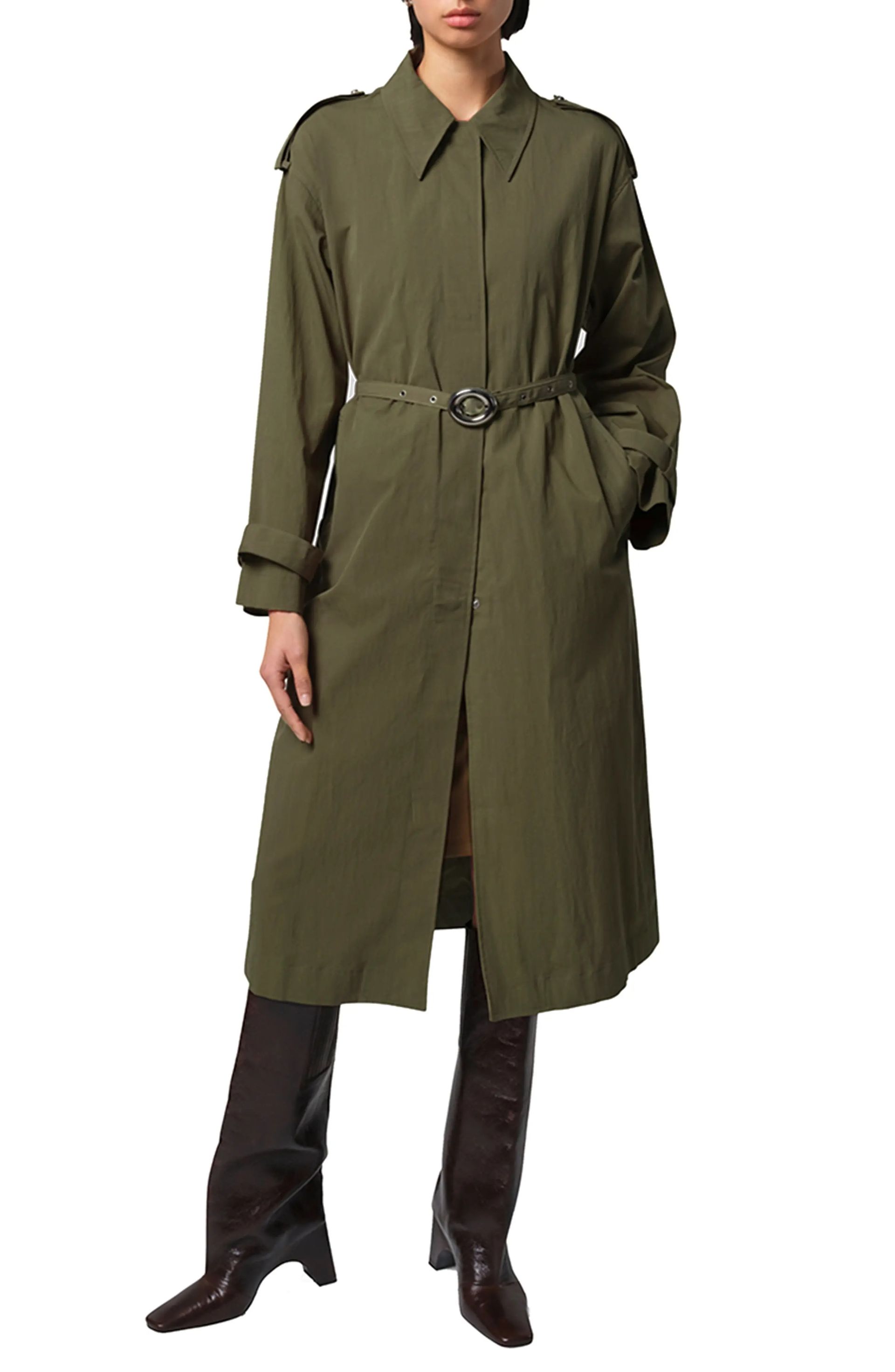 A woman wearing an olive green trench coat and black boots