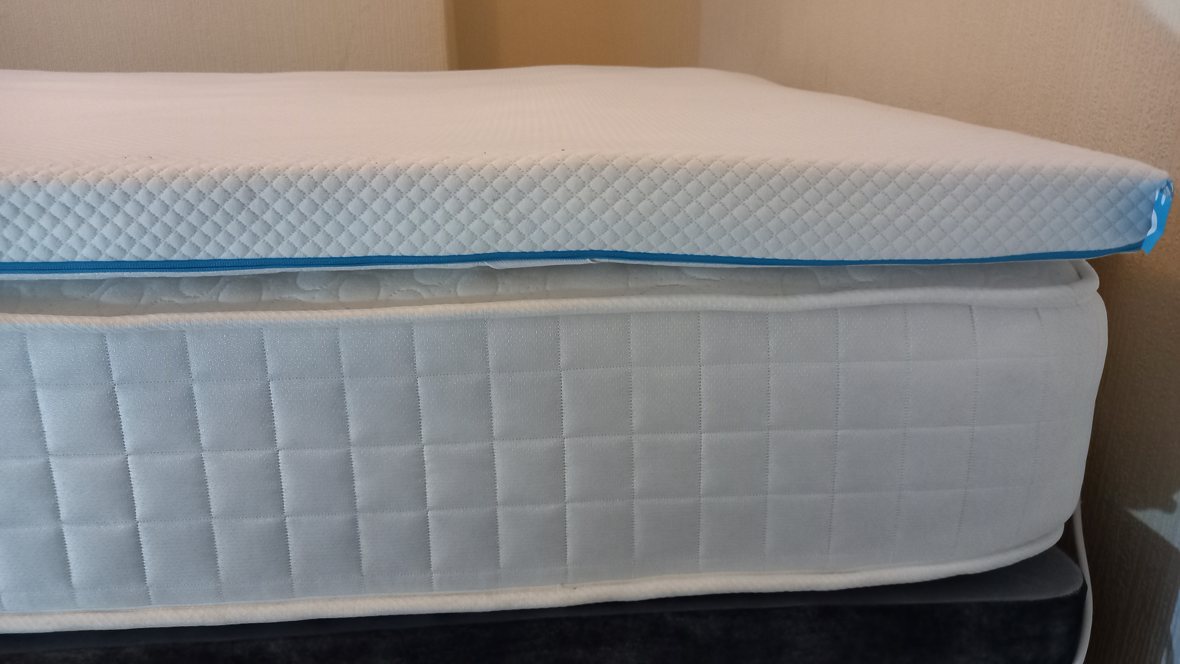 Side-on view of the Simba Cool Foam Mattress Topper sitting on top of a mattress, showing the 6.5cm depth and the distinctive teal zip running along the edge.