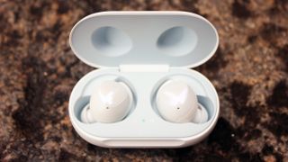 A pair of Samsung Galaxy Buds in white in their charging case on a brown surface