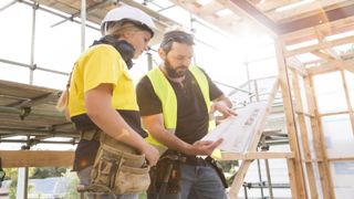 Builders discussing works plan surrounded by timber frames